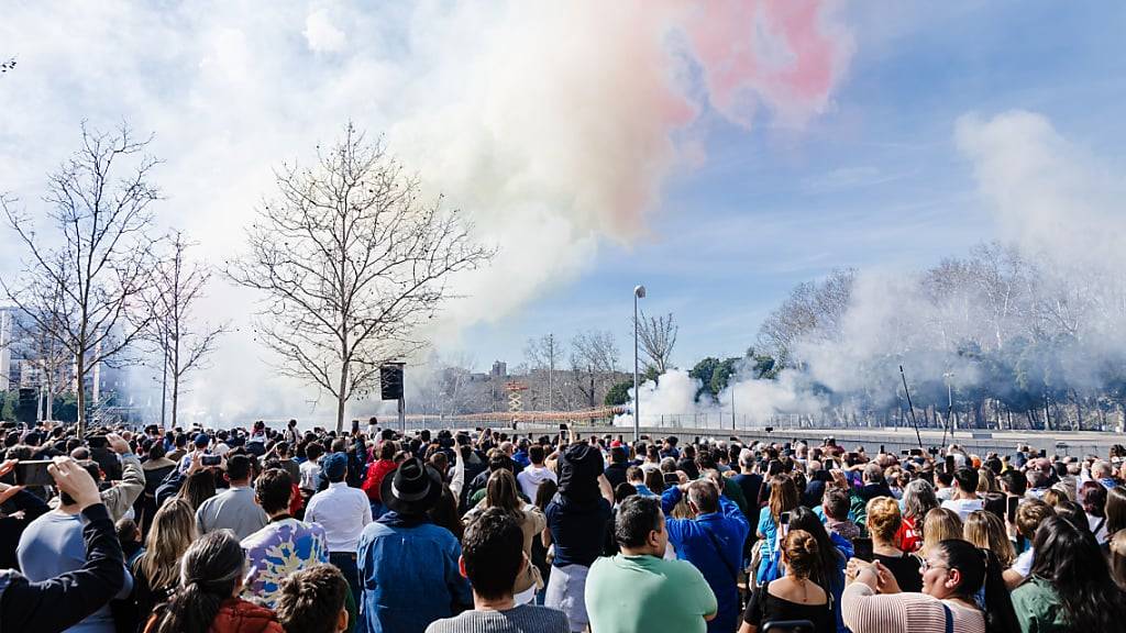 Zuschauer beobachten den bunten Rauch während der ersten Madrider Mascleta auf der Puente del Rey. Bei der Veranstaltung, die von der Pirotecnia Valenciana durchgeführt wird, werden 300 Kilo Schießpulver für insgesamt sieben Minuten mit 3.000 Detonationen gezündet. Die Regierungsdelegation hat die Mascleta schließlich genehmigt, obwohl Umweltschutz- und Umweltorganisationen vor Gericht geklagt haben. Foto: Carlos Luján/EUROPA PRESS/dpa
