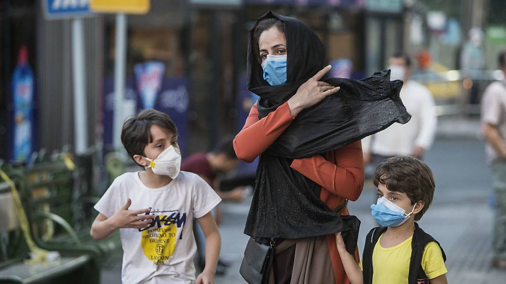 Kinder mit Gesichtsmasken gehen mit ihrer Mutter eine Straße entlang. Der Iran meldete am 21. Juli eine neue Rekordzahl an Corona-Toten. Foto: Ahmad Halabisaz/XinHua/dpa