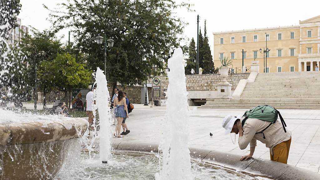 Ein Mann erfrischt sich an einem  Springbrunnen auf dem Syntagma-Platz in Athen. Foto: Socrates Baltagiannis/dpa