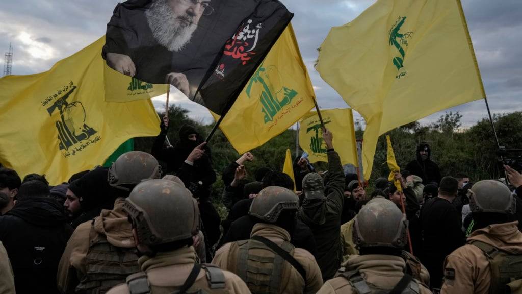 ARCHIV - Die libanesische Armee steht Wache, während Hisbollah-Anhänger mit Fahnen der Partei und einem Bild des getöteten Hisbollah-Führers Hassan Nasrallah eine Straßenverbindung zum internationalen Flughafen blockieren. Foto: Bilal Hussein/AP/dpa
