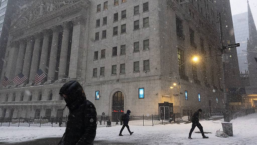 Menschen gehen während eines Schneesturms an der New Yorker Börse in der Wall Street vorbei. Foto: Mark Lennihan/AP/dpa