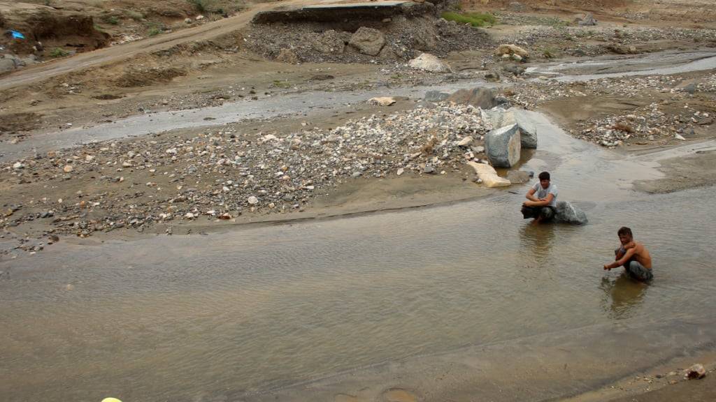 Männer sitzen in der Nähe einer teilweise eingestürzten Straße in der Nähe der Stadt Abs im Südwesten Jemens, nachdem schwere saisonale Regenfälle im Land zu Überschwemmungen geführt haben. Foto: Eissa Ahmed/AP/dpa