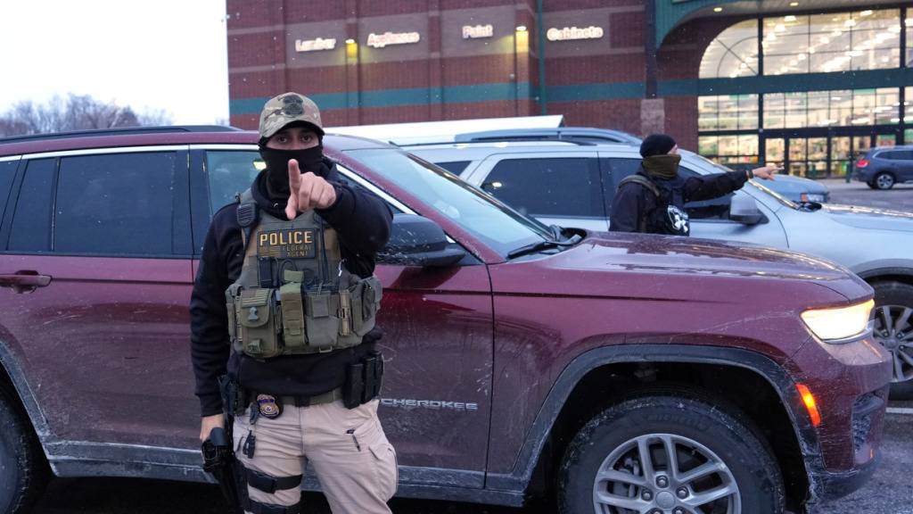 Ein ICE-Beamter warnt einen Fotografen, zurückzubleiben, während eine Person festgenommen wird. Foto: Adam Gray/AP/dpa