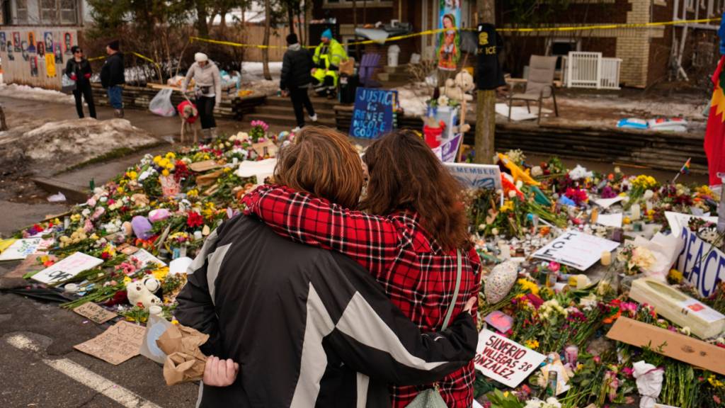 Menschen umarmen sich beim Besuch einer behelfsmäßigen Gedenkstätte für Renee Good, die letzte Woche von einem ICE-Beamten erschossen wurde. Nach den tödlichen Schüssen auf eine Frau in Minneapolis halten die Proteste gegen die US-Einwanderungsbehörde ICE an. Foto: John Locher/AP/dpa