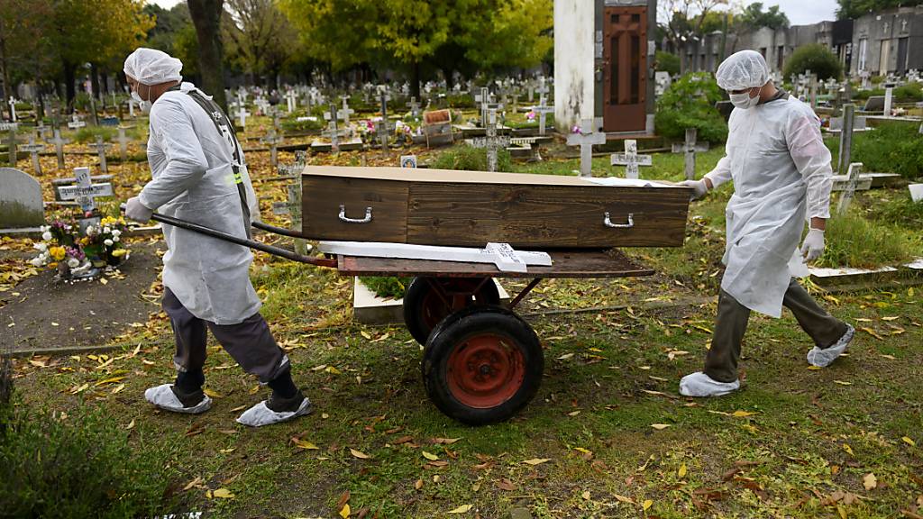 Zwei Männer in Schutzanzügen transportieren den Sarg mit dem Leichnam eines Corona-Opfers. Trotz restriktiver Ausgangsbeschränkungen haben sich in Argentinien mehr Menschen als jemals zuvor seit Beginn der Pandemie vor über einem Jahr mit dem Coronavirus infiziert. Foto: Mario De Fina/AP/dpa