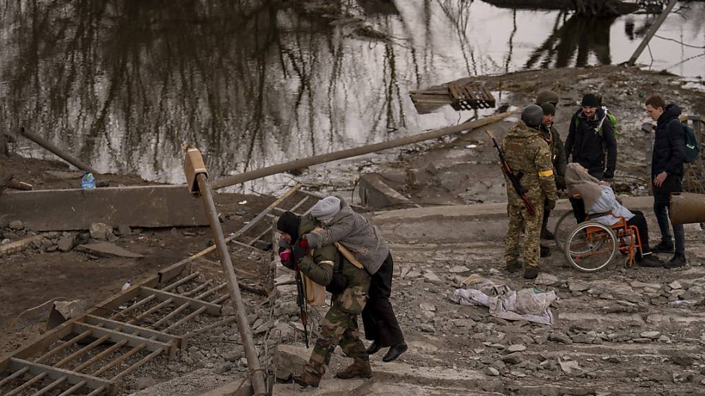 Ein ukrainischer Soldat trägt eine ältere Frau über einen Fluss bei Irpin am Stadtrand von Kiew. Foto: Emilio Morenatti/AP/dpa