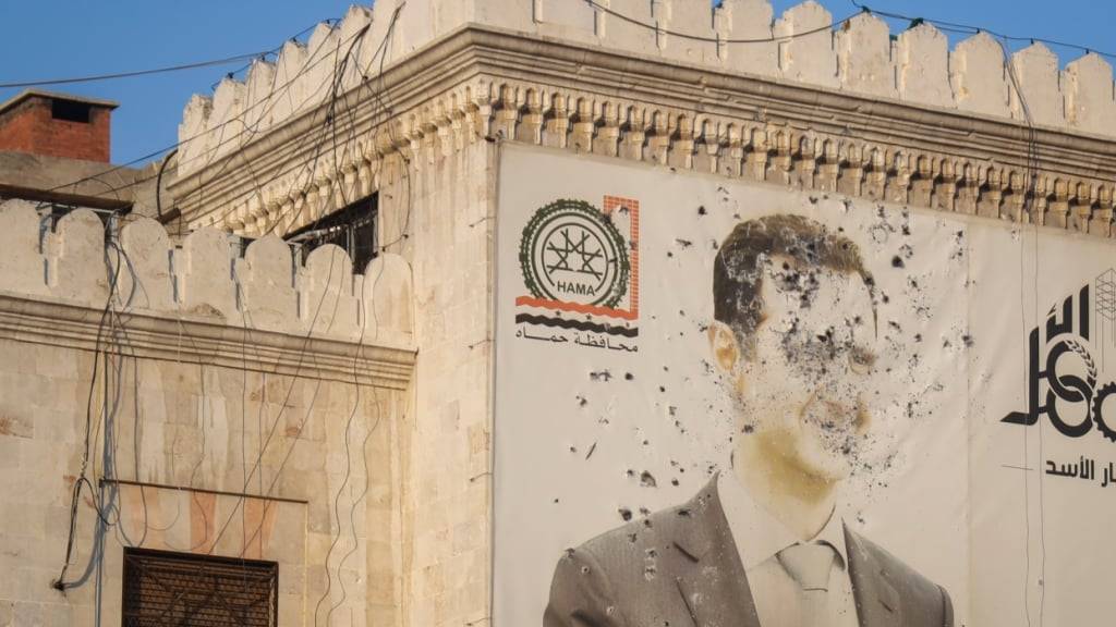 ARCHIV - Ein Bild des syrischen Präsidenten Baschar al-Assad, durchlöchert von Kugeln, ist auf der Fassade des Büros der Provinzregierung nach der Übernahme der Stadt Hama durch aufständische Kämpfer zu sehen. Foto: Omar Albam/AP/dpa