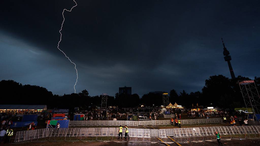 dpatopbilder - Ein Blitz ist am dunklen Himmel in der Fanzone in Dortmund zu sehen. Foto: Friso Gentsch/dpa