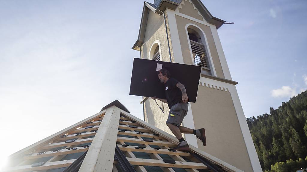 Arbeiter montieren Solarpanels auf dem Dach der historischen reformierten Kirche in Trin, einem Bündner Bergdorf am Rand der Ferienregion Flims-Laax.