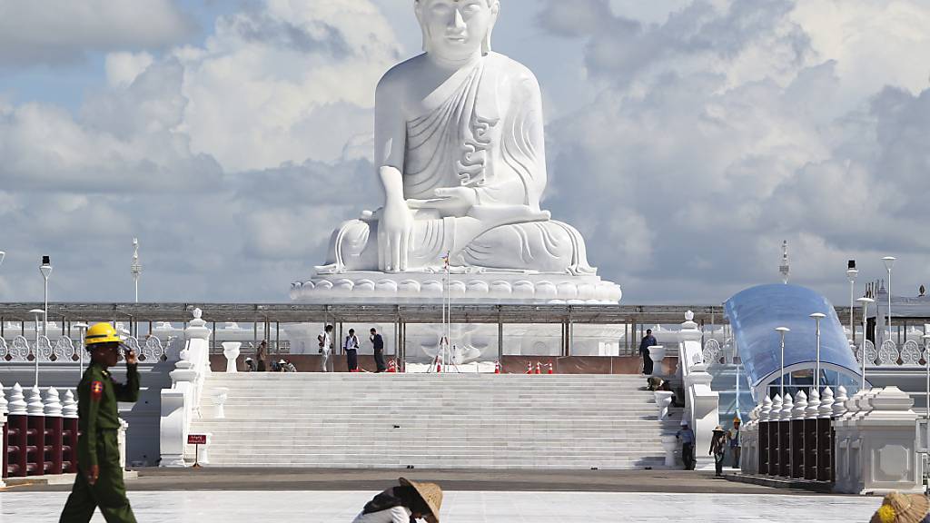 Ein Soldat geht an Frauen vorbei, die unterhalb der Marmorstatue des Maravijaya-Buddha arbeiten. Foto: Aung Shine Oo/AP/dpa