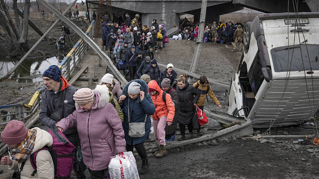 Menschen überqueren den Fluss Irpin auf einem improvisierten Weg unter einer durch einen russischen Luftangriff zerstörten Brücke, während sie aus der Stadt Irpin fliehen. Foto: Vadim Ghirda/AP/dpa