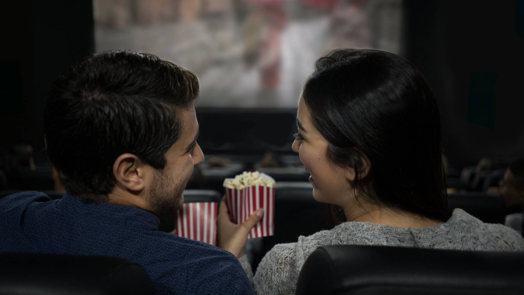 Happy Latin American couple lauging at the movies eating popcorn and having fun