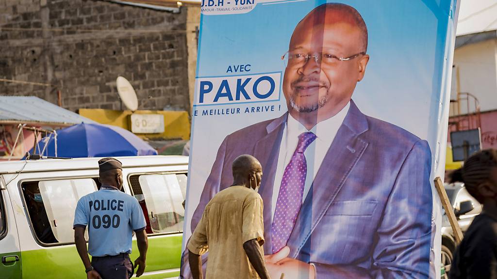 Menschen gehen an einem Wahlplakat des oppositionellen Präsidentschaftskandidaten Guy Brice Parfait Kolelas vorbei. Foto: Lebon Chansard Ziavoula/AP/dpa