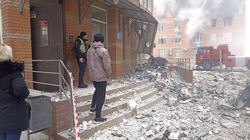 Anwohner und ein ukrainischer Soldat beobachten, wie Feuerwehrleute ein Feuer in einem beschädigten Wohnhaus infolge eines russischen Luftangriffs löschen. Foto: Artem Perfilov/AP/dpa