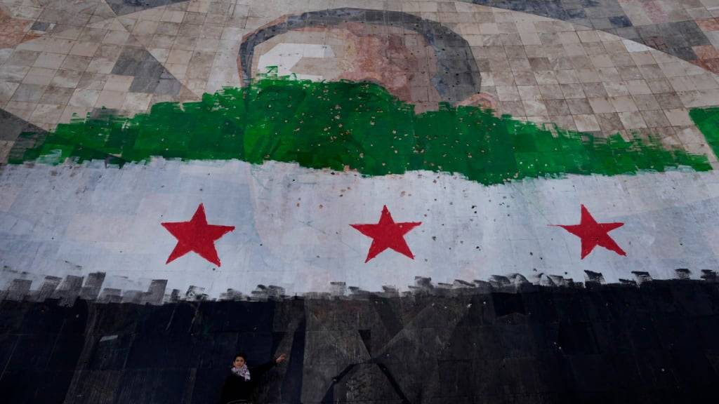 ARCHIV - Ein riesiges Porträt des verstorbenen syrischen Präsidenten Al-Assad, übermalt mit den Farben der sogenannten «revolutionären» Flagge, in Damaskus. Foto: Hussein Malla/AP/dpa