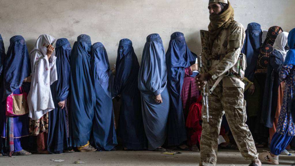 ARCHIV - Ein Taliban-Kämpfer steht Wache, während Frauen in Kabul darauf warten, Lebensmittelrationen zu erhalten, die von einer humanitären Hilfsgruppe verteilt werden. Foto: Ebrahim Noroozi/AP/dpa