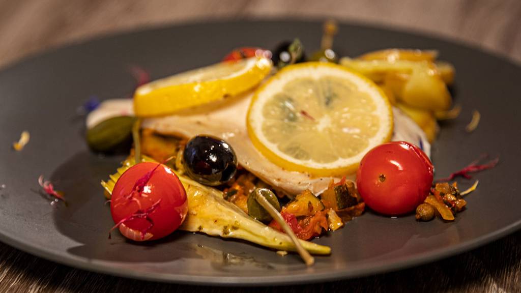 HAUPTGANG: WOLFSBARSCH AUS DEM OFEN MIT CHERRY-TOMATEN, ARTISCHOCKEN-HERZE, SCHWARZE OLIVEN UND KAPERN MIT KNUSPRIGEN KARTOFFELSCHEIBEN