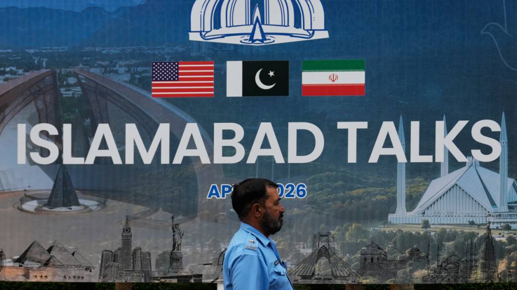 Ein Polizeibeamter geht vor einem Medienzentrum an einer Plakatwand zu den Verhandlungen zwischen den USA und dem Iran vorbei. Foto: Anjum Naveed/AP/dpa