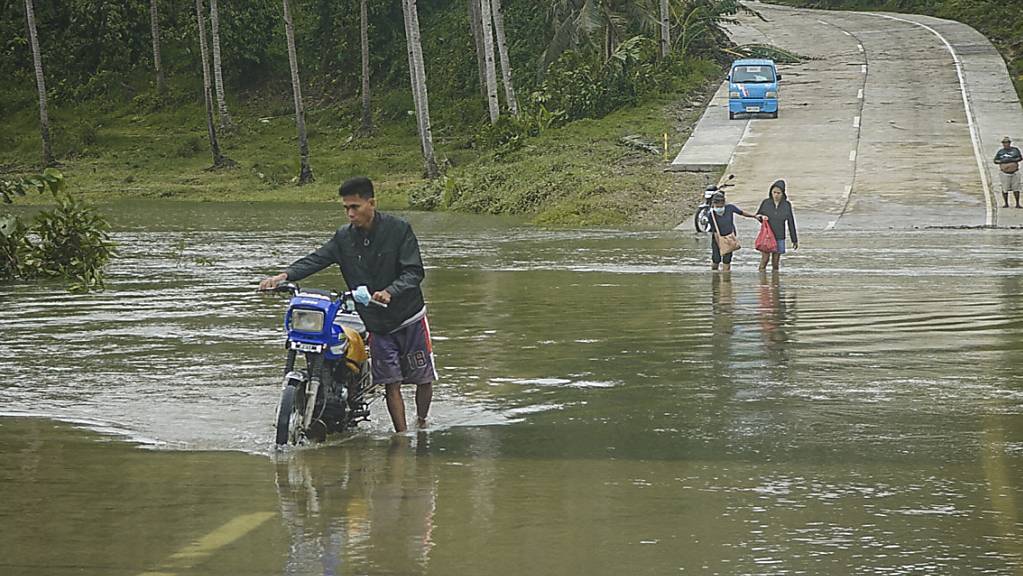 Bewohner überqueren eine überflutete Straße auf den Philippinen. Die Überflutungen wurden durch den Regen des Taifuns «Surigae» verursacht, der bisher mindestens sieben Menschenleben gefordert hat. Foto: Uncredited/AP/dpa