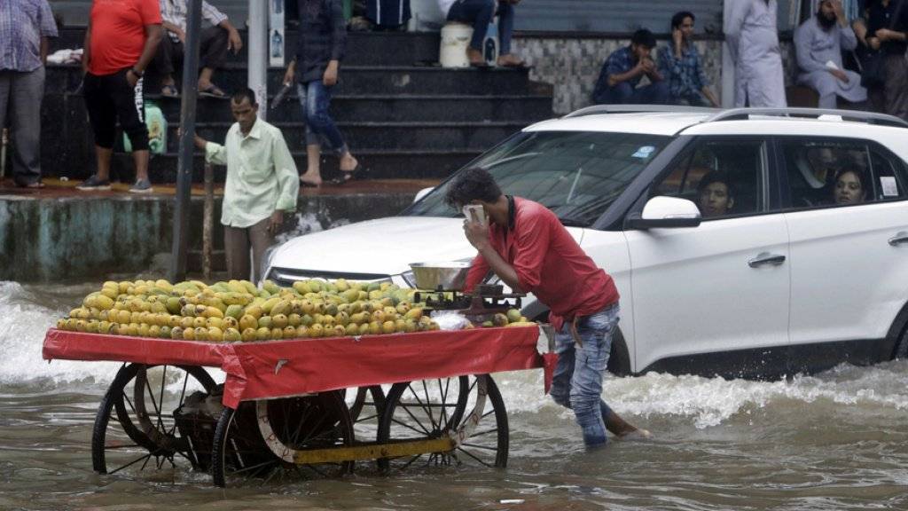 Ein Strassenhändler schiebt seinen Wagen durch die überschwemmten Strassen von Mumbai.