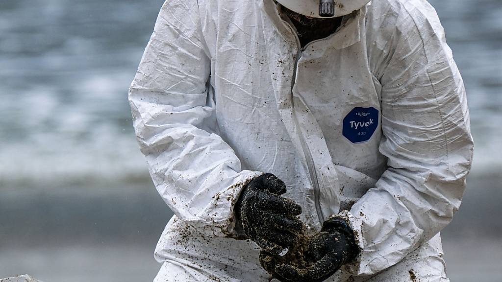 Ein Arbeiter in einem Schutzanzug säubert einen Strandabschnitt. Foto: Jason Ryan/ZUMA Press Wire Service/dpa