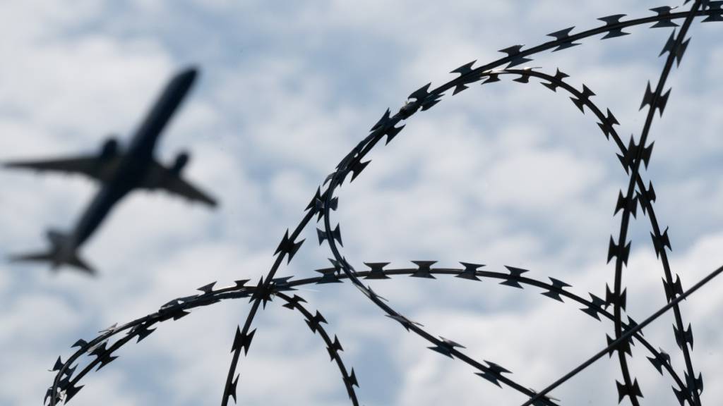 ARCHIV - Ein Flugzeug hebt am Flughafen BER hinter einem Zaun mit Natodraht ab. Foto: Sebastian Gollnow/dpa