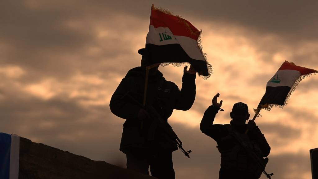 ARCHIV - Kämpfer von Milizen im Irak, die vom Iran unterstützt werden, schwenken irakische Flaggen. Foto: Anmar Khalil/AP/dpa