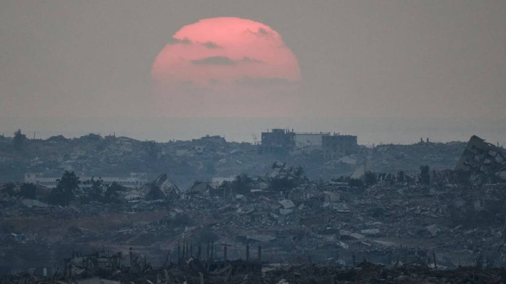 ARCHIV - Die Sonne geht hinter zerstörten Gebäuden im Gazastreifen unter (Archivbild). Foto: Leo Correa/AP/dpa