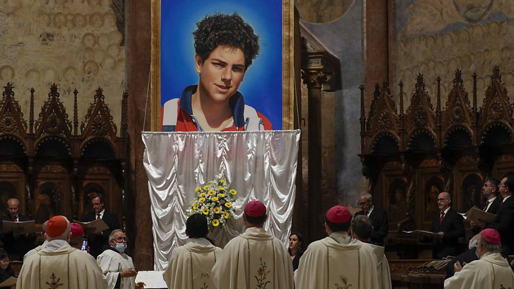 Ein Foto des 15-jährigen Carlo Acutis, der 2006 an Leukämie verstorben ist, wird bei seiner Seligsprechung in der Basilika San Francesco enthüllt. Foto: Gregorio Borgia/AP/dpa