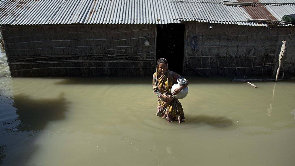 Eine Frau watet im indischen Bundesstaat Assam durch die Fluten.