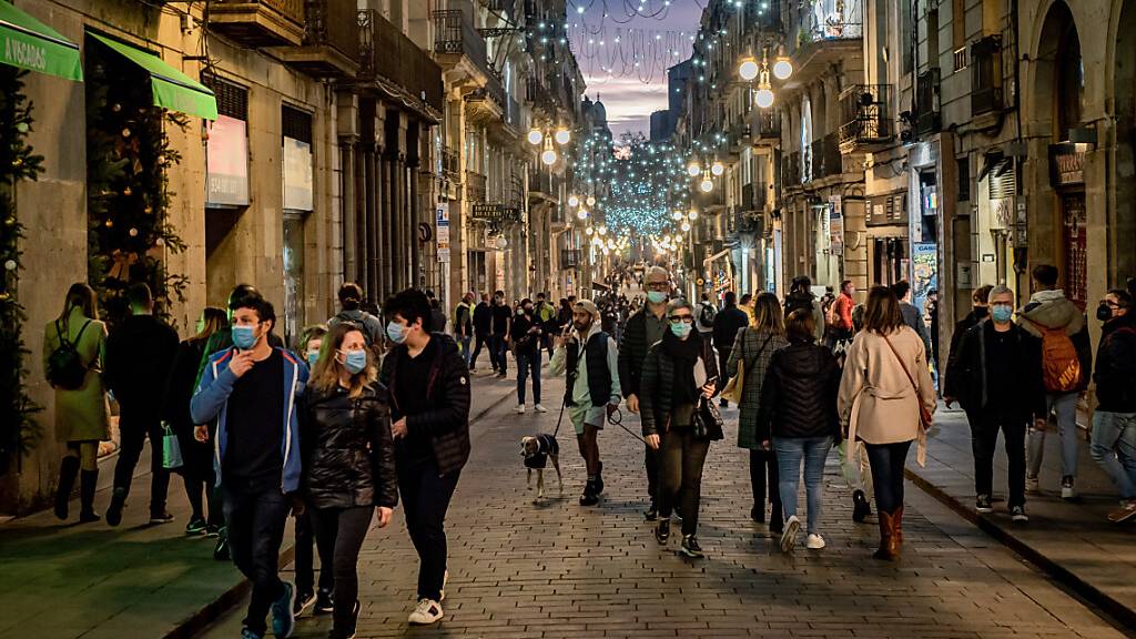 Menschen gehen eine beleuchtete Straße in Barcelona entlang. Trotz einer hohen Impfquote von rund 80 Prozent klettert auch in Spanien die Zahl der Corona-Infektionen weiter rasant. Foto: Jordi Boixareu/ZUMA Press Wire/dpa