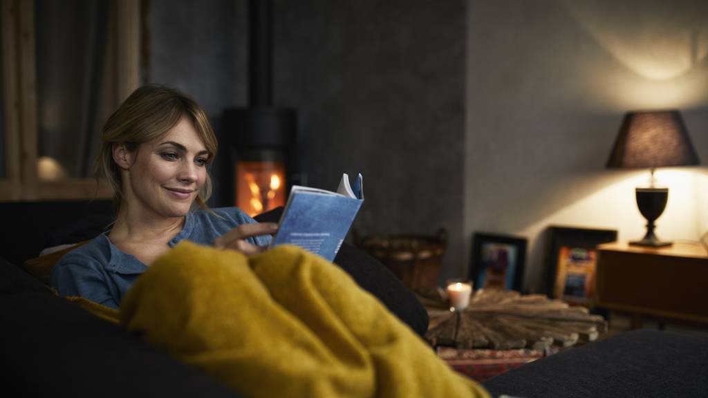 Frau sitzt auf der Couch und liest ein Buch. 