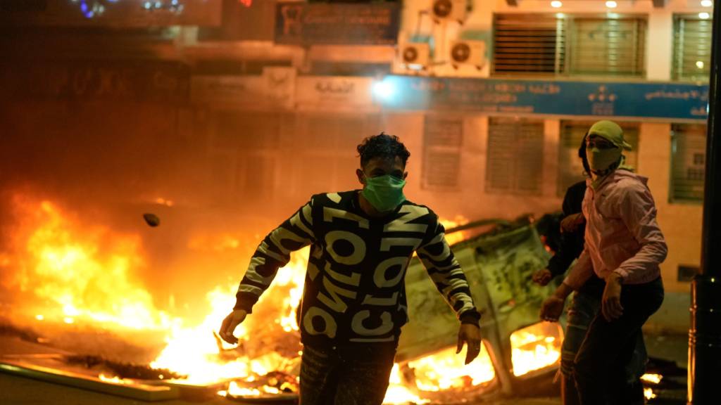 dpatopbilder - Personen stehen neben einem abgefackelten Polizeifahrzeug, als die von Jugendlichen angeführten Proteste für Reformen im Gesundheits- und Bildungswesen in Gewalt umschlugen. Foto: Mosa'ab Elshamy/AP/dpa