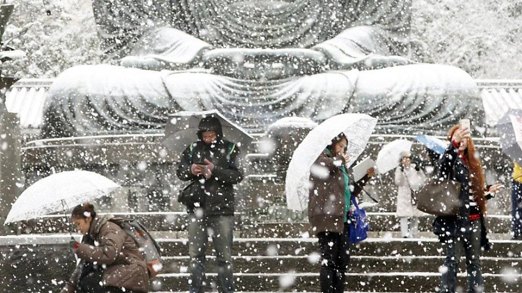 Japanerinnen und Japaner im Schnee am Fuss einer Buddha-Statue nahe Tokios