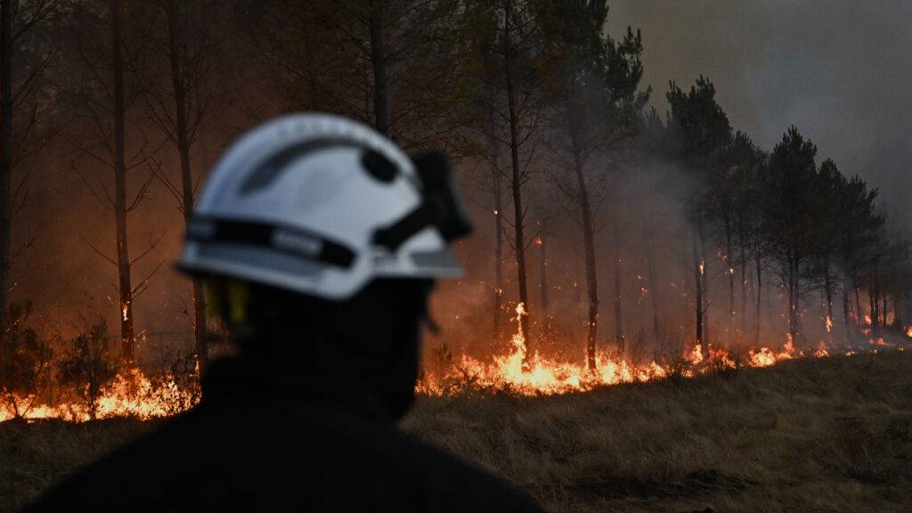ARCHIV - Ein Feuerwehrmann geht vor brennenden Bäumen vorbei, während in der Nähe von Marcheprime, außerhalb von Bordeaux, Frankreich, ein Waldbrand wütet. Foto: Emma Da Silva/AP/dpa (Archivbild)