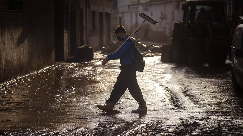 Ein Freiwilliger geht mit einem Besen über eine schlammige Straße. Foto: Emilio Morenatti/AP/dpa