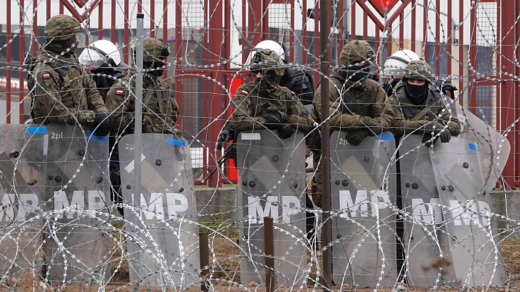 Polnische Sicherheitskräfte stehen hinter dem Grenzzaun am Grenzübergang Brusgi (Belarus) und Kuznica (Polen). Foto: Ulf Mauder/dpa