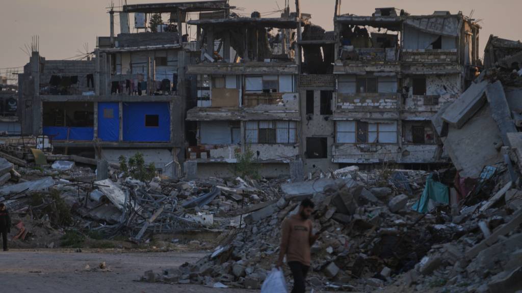 ARCHIV - Palästinenser gehen im südlichen Gazastreifen eine Straße entlang, die von Gebäuden umgeben ist, die bei israelischen Luft- und Bodenoperationen zerstört wurden. Foto: Abdel Kareem Hana/AP/dpa/Archivbild