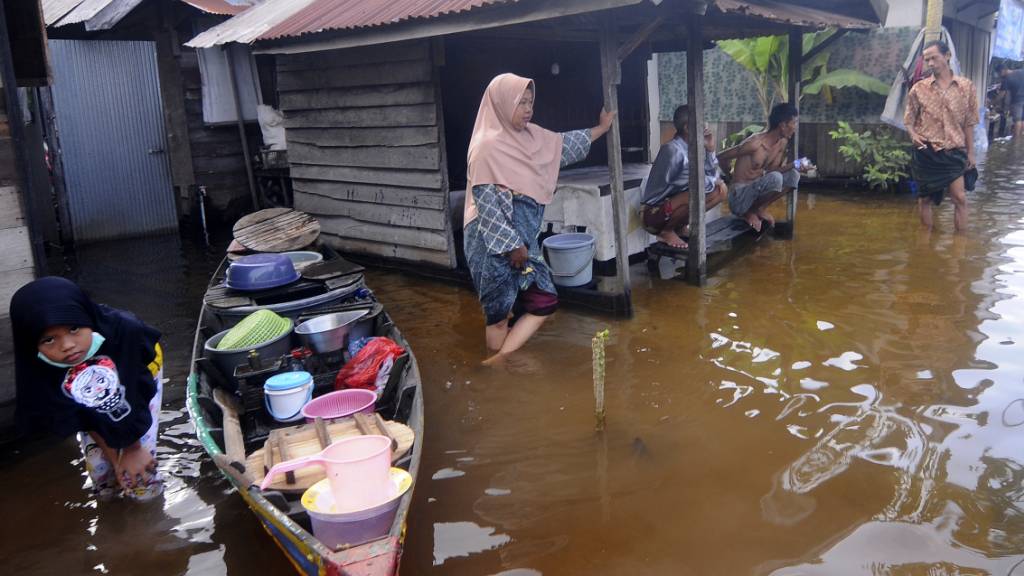 Anwohner stehen auf der überfluteten Straße vor ihren Häusern auf der indonesischen Insel Borneo. Foto: Iman Satria/AP/dpa