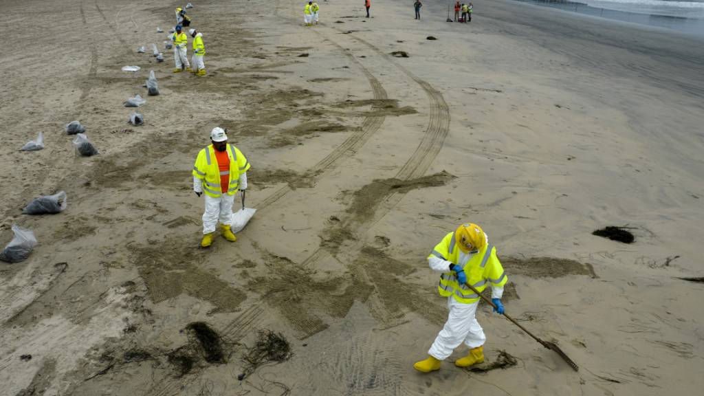 Arbeiter in Schutzanzügen säubern einen vom ausgetretenen Öl verunreinigten Strand in Newport Beach in Kalifornien. Foto: Ringo H.W. Chiu/AP/dpa