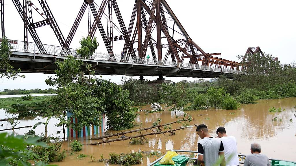 Menschen beobachten den überfluteten Roten Fluss neben der ikonischen Long Bien-Brücke nach dem Taifun Yagi. Foto: Huy Han/AP/dpa