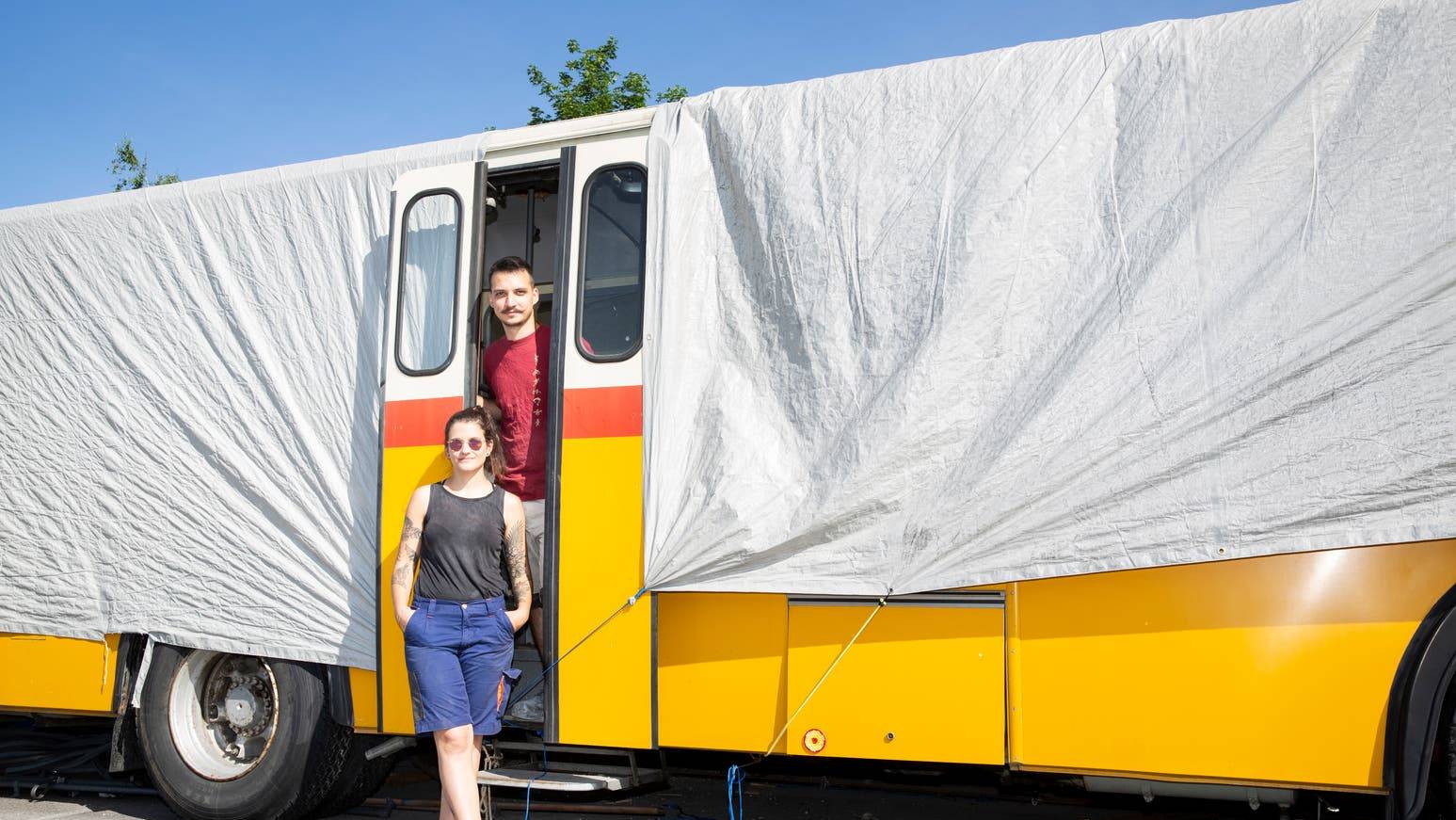 Das ausgehöhlte Postauto unter der Plane: Astrid Dörig und Samuel Rohrhirs stehen vor ihrem Projekt.