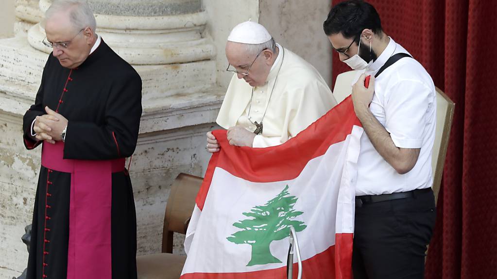 Papst Franziskus (M) hält bei seiner ersten Generalaudienz mit Gläubigen seit Ausbruch der Corona-Pandemie in Gedenken an die Opfer der Explosion die Flagge des Libanon. Foto: Andrew Medichini/AP/dpa