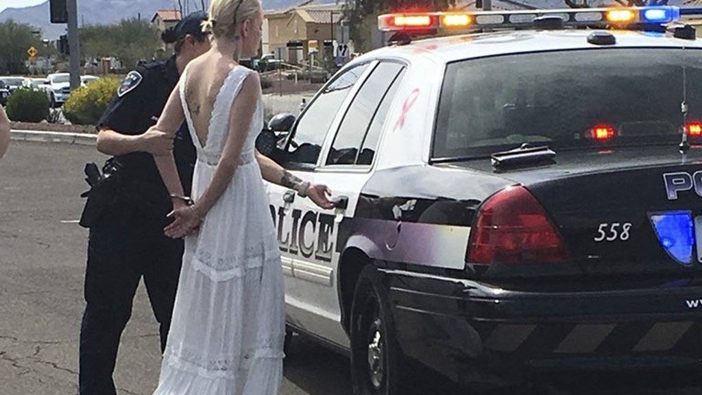 Die Braut wird in Handschellen zu einem Polizeiauto gebracht.