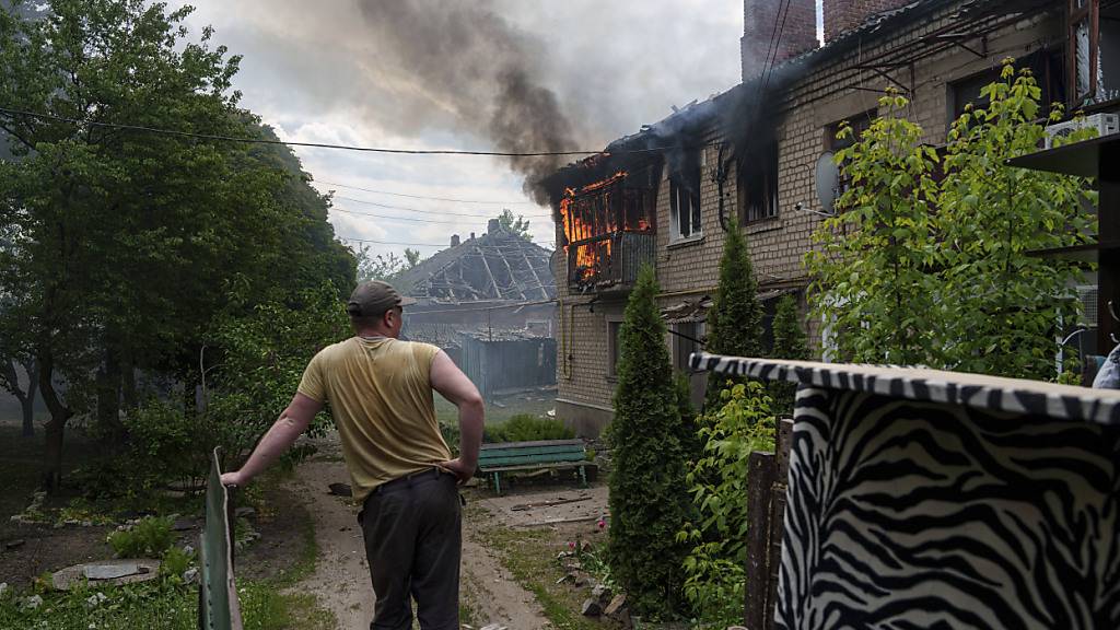 Ein Anwohner betrachtet ein brennendes Haus nebenan nach einem russischen Luftangriff auf Wowtschansk. Foto: Evgeniy Maloletka/AP/dpa