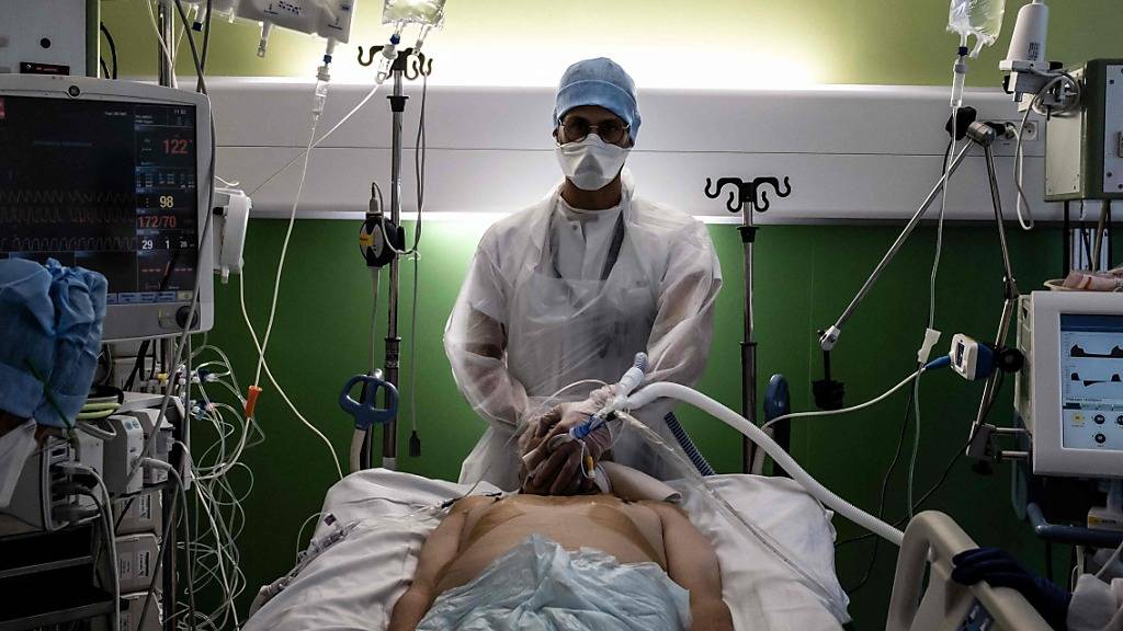 Ein medizinischer Angestellter (M) kümmert sich in der Intensivstation des Krankenhauses Lyon-Süd in Pierre-Benite um einen Corona-Patienten. Foto: Jeff Pachoud/AFP/dpa