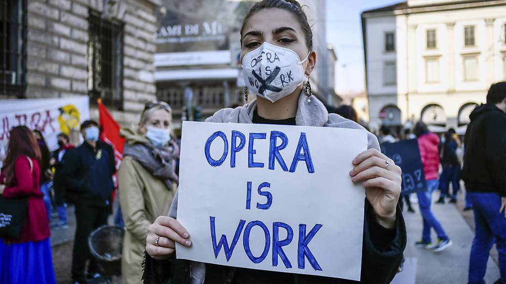 Eine Frau mit Mundschutz hält bei einer Demonstration gegen die Maßnahmen der Regierung zur Eindämmung der Corona-Pandemie ein Schild mit der Aufschrift «Opera is work» (zu deutsch: «Oper ist Arbeit») in den Händen. Foto: Claudio Furlan/LaPresse/AP/dpa
