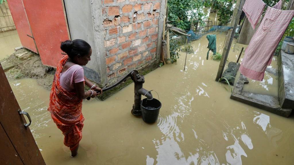 Eine Frau in Indien benutzt eine Handpumpe, um Wasser inmitten der überfluteten Umgebung ihres Hauses nach tagelangen sintflutartigen Monsunregenfällen zu sammeln. Foto: AP/dpa