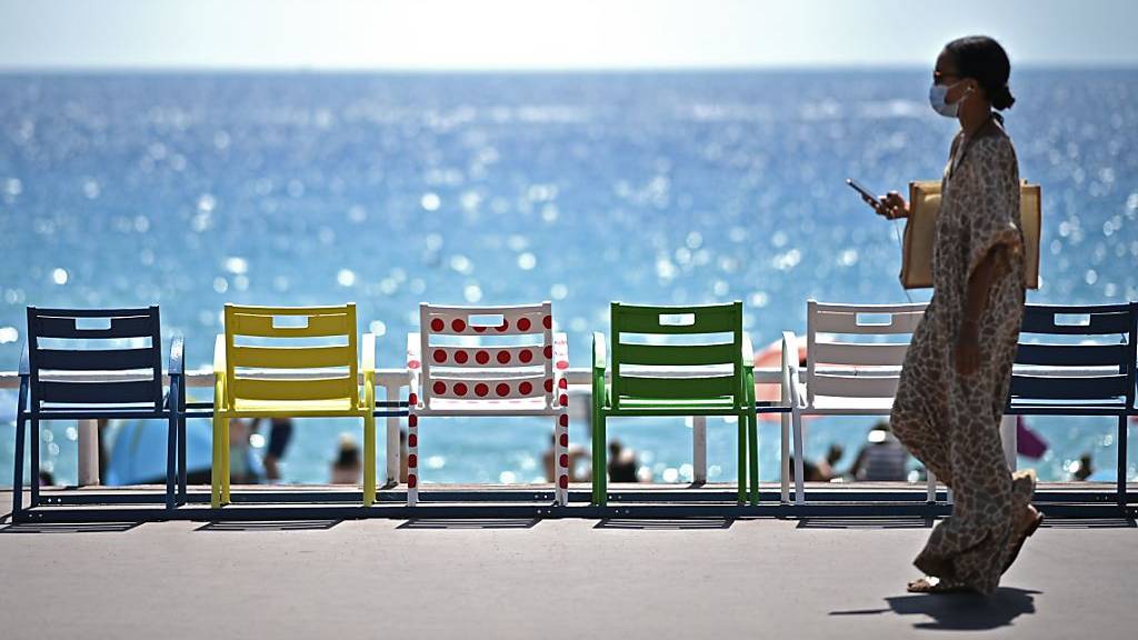 Eine Frau geht auf der Strandpromenade an der französischen Riviera an Stühlen vorbei.
