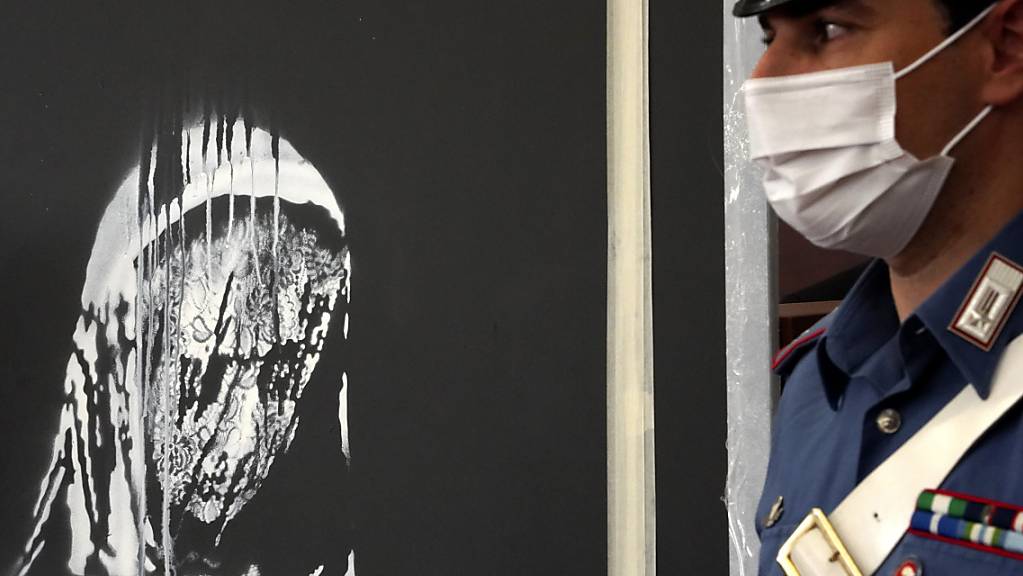 Ein Beamter der Carabinieri steht neben der gestohlenen Tür aus der Pariser Konzerthalle Bataclan, auf der ein dem Streetart-Künstler Banksy zugeschriebenes Graffiti zu sehen ist. Foto: Andrea Rosa/AP/dpa - ACHTUNG: Nur zur redaktionellen Verwendung im Zusammenhang mit der aktuellen Berichterstattung und nur mit vollständiger Nennung des vorstehenden Credits